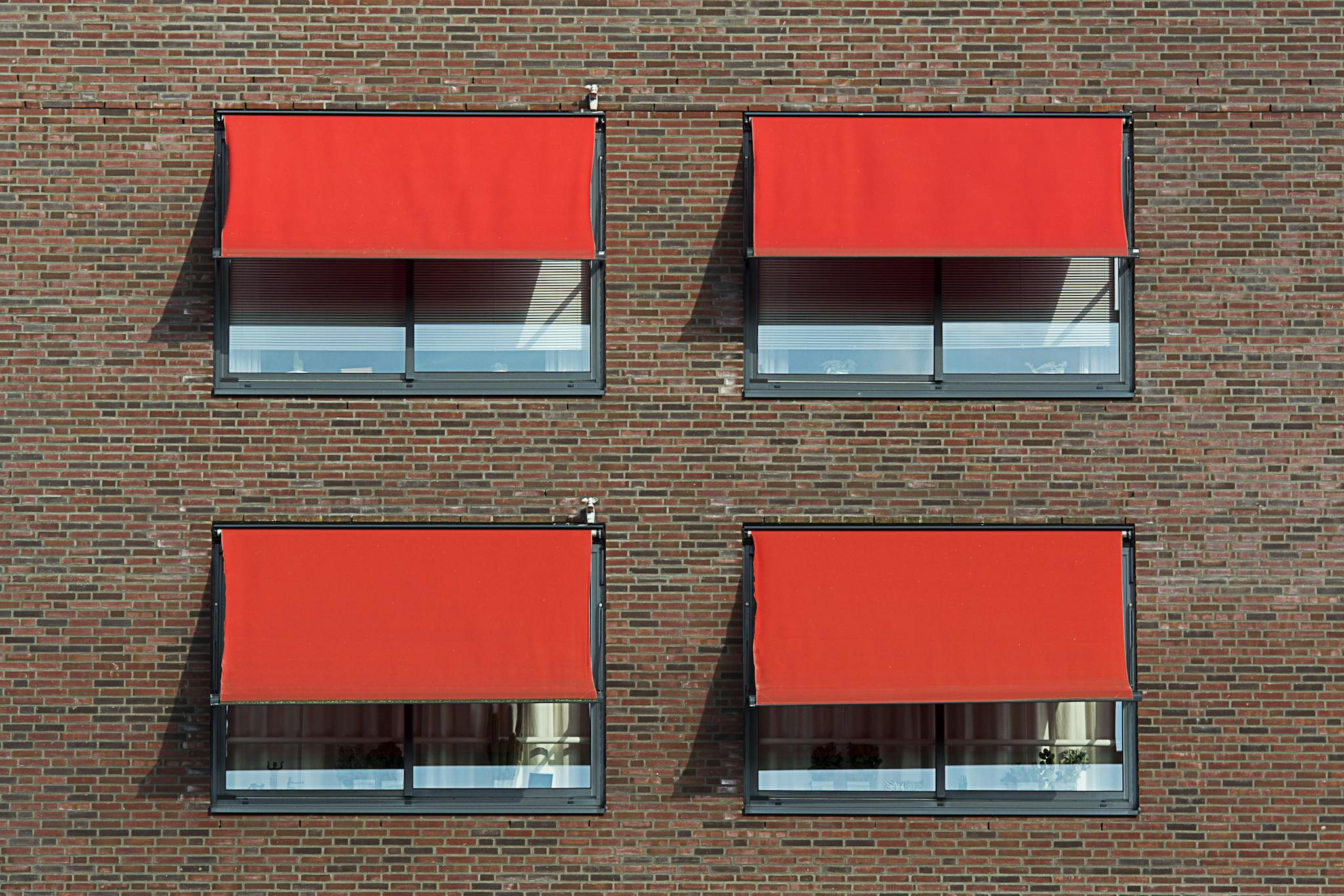 Symmetrical brick wall with four red sun shades covering windows.